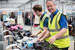 Two men sorting clothes on conveyor belt in warehouse