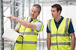 Two men in warehouse, one pointing with pen