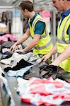 Two men in warehouse sorting clothing on conveyor belt