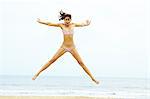 Young woman in bikini doing star jump on beach
