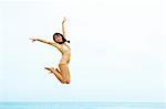 Young woman in bikini jumping on beach