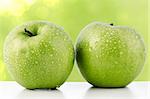 Two fresh green apples on green defocused background.