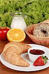 Breakfast with a croissant and strawberry jam. Served with oranges, apple and bagels.