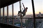 Industrial climber looking through a window while hanging on a rope outside a high building