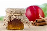 Peach jam with fruit and cinnamon over raffia on white background.