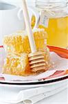 Sweet honeycombs and honey stick on a red rustic plate.