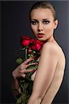 pretty blonde girl's low key portrait with three red roses, her body is turned in profile,  looks in to the lens and she takes the roses near the face