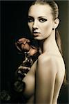 pretty blonde girl's low key portrait with three red roses, her body is turned in profile, looks in to the lens and she takes the roses with right hand