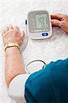 Closeup of a senior man's arm hooked up to a home blood pressure machine, showing his results.