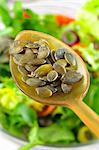 Graines de citrouille sur une cuillère au-dessus d'un bol de salade