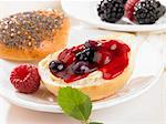 A bread roll spread with butter and berry jam