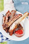 A person holding a plate of grilled spare ribs and barbecue sauce