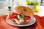 A sesame seed bagel with brie, ham and tomatoes