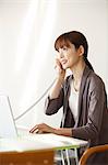 Femme japonaise parlait au téléphone fixe tout en travaillant sur ordinateur portable