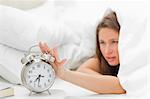 Woman in her bed turning off her alarm clock