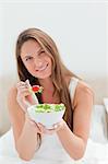 Close-up of a woman with a bowl of salad offering a tomato to eat