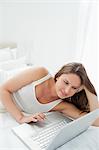 Close-up of a woman lying on her bed while using a laptop