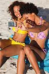 Junge Frau, die sich selbst und einem Freund beim Sitzen am Strand fotografieren