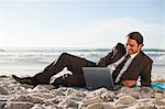 Smiling Businessman liegend auf der Seite am Strand