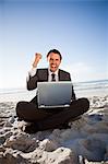 Successful businessman sitting on the beach while raising his fist