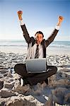 Happy businessman raising his arms in success while sitting on the beach