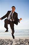 Young businessman shouting while jumping on the beach
