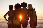 Young four women holding each other while standing on the beach