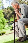 Old man sitting down resting his hands on his walking stick