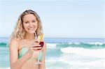 Woman smiling while holding a cocktail by the sea