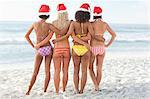 Four friends wearing Santa hats looking at the sea