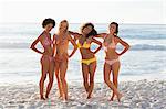 Four friends leaning on each other while smiling as they stand on the beach