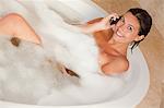 Smiling woman lying in the tub with her cellphone