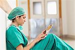 Femme chirurgien assis sur un couloir tout en tenant une tablette tactile