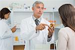 Pharmacist pointing at a flask of pills in front of a customer