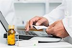 Pharmacist holding a prescription while typing on a computer on a desk