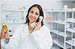 Pharmacist holding a bottle of pills while phoning