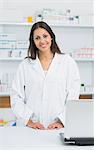 Smiling female pharmacist standing behind the counter of a pharmacy