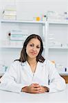 Smiling female pharmacist joining her hands on the counter of a pharmacy