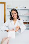 Happy female pharmacist receiving a prescription from a customer