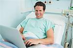 Patient typing on a laptop while lying on a bed and laughing