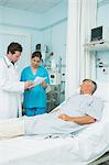 Male doctor and female nurse holding a sheet of paper in the room of patient