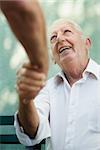 Active retirement, two old male friends talking and shaking hands on bench in public park