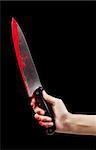 A bloody hand holding a large blood covered knife on a black isolated background.