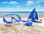 Goggles and toy sailboat in sand at the beach scene