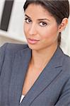 Beautiful young Latina Hispanic woman or businesswoman in smart business suit sitting at a desk in an office