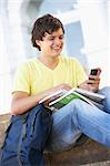 Male Teenage Student Sitting Outside On College Steps Using Mobile Phone