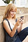 Unhappy Female Teenage Student Sitting Outside On College Steps Using Mobile Phone