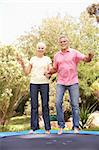 Senior Couple Jumping On Trampoline In Garden