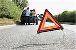 Couple Broken Down On Country Road With Hazard Warning Sign In Foreground