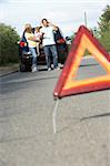 Family Broken Down On Country Road With Hazard Warning Sign In Foreground